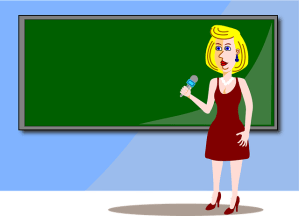 Lehrerin vor Tafel mit Mikrofon in der Hand.