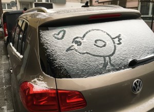 Vogel in Schnee gemalt, der auf Heckscheibe von Auto liegt.