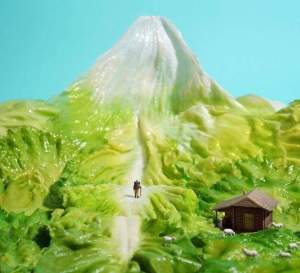 Miniaturfigur wandert auf Salatblatt, das wie eine Graslandschaften mit Gletscher in der Ferne aussieht. 