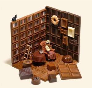 Miniaturfigur sitzt mit Buch zwischen Schokoladentafeln, die wie die Wände einer dunkel getäfelten Bibliothek aussehen.