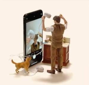 Miniaturmann steht vor Handy und benutzt Ohrstecker als Fön.