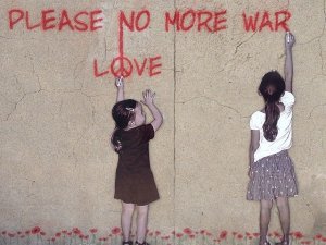 Zwei Mädchen schreiben an Hauswand als Graffito „Please no more war - Love“.
