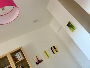 Ausschnitt von Zimmer mit Bildern, Deckenlampe und Bücherregal, von unten fotografiert.