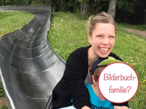 Mutter fährt mit Jungen lachend auf einer Sommerrodelbahn.