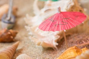 Papierschirmchen am Strand mit Muscheln im Hintergrund.