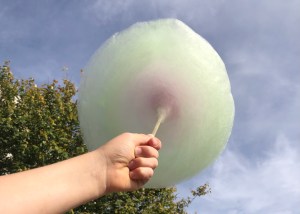Kinderhand hält bunte Zuckerwatte. Blauer Himmel im Hintergrund.